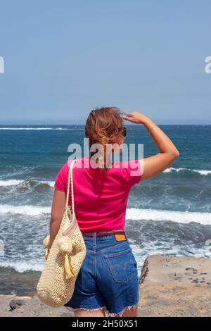Carefree young millennial woman wearing short blue jeans and a bright t-shirt, with an oversized beach bag on the shoulder Stock Photo