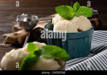 Vanilla icecream balls in clay bowls on wooden kitchen table with ice cream scoop aside Stock Photo