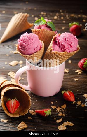 Wafer cones with strawberry icecream in pink mug on wooden kitchen table Stock Photo