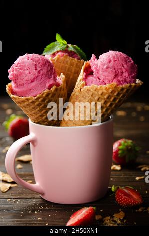 Wafer cones with strawberry icecream in pink mug on wooden kitchen table Stock Photo