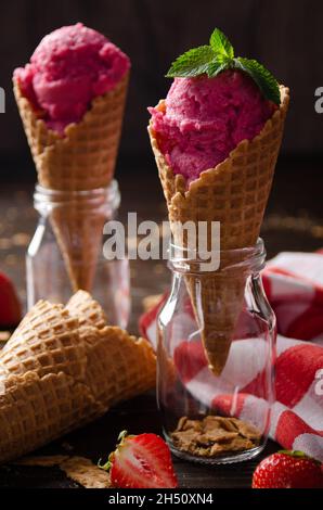 Wafer cones with strawberry icecream in two glass bottles on wooden kitchen table Stock Photo