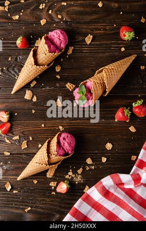 Wafer cones with strawberry icecream on wooden kitchen table with crumbs and berries aside Stock Photo