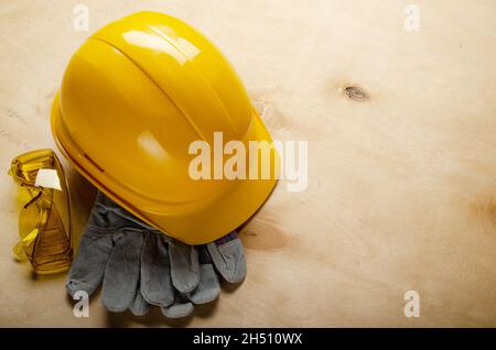 Yellow plastic hard hat glasses and protective gloves laying on plywood. Safe labor concept Stock Photo