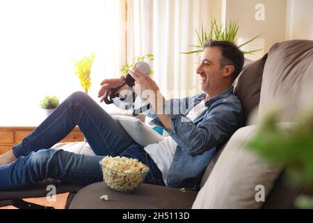 Man getting ready to watch a movie in a virtual reality glasses sitting on the couch at home with popcorn Stock Photo