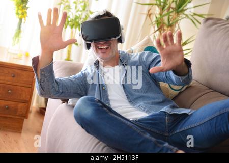 Man using virtual reality glasses lying on a sofa in the living room at home Stock Photo