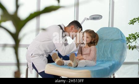 A caring doctor examines a little girl's ear using a special device. Stock Photo