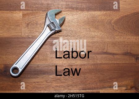 a flexible chromed adjustable wrench lies on a dark wooden table. The words labor law are written on the table in black letters Stock Photo
