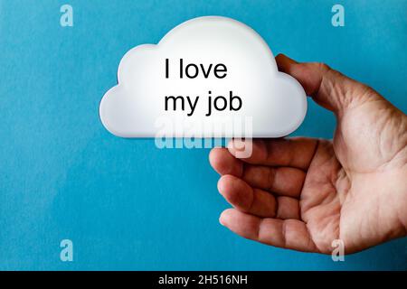 Hand holds a white cloud symbol against a blue background. The text is written on the cloud: I love my job Stock Photo