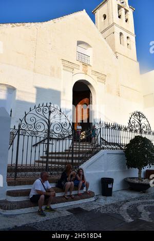 Frigiliana - Spain - August 18 2018 :  Historic old church in the village square  Holiday makers relax in the warm late afternoon by the historic buil Stock Photo