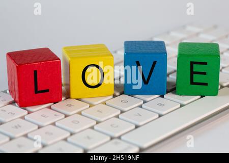 The letters LOVE are written on blocks. These letters are written in white on red, yellow, blue and green blocks and stand on a bright computer keyboa Stock Photo