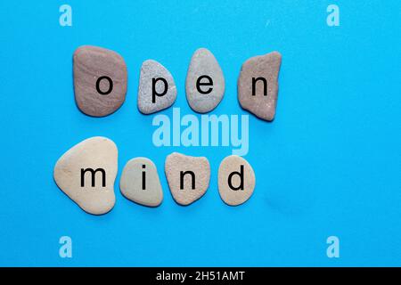 The word open mind is written on polished natural stones that are true to color. The words are isolated on a blue background Stock Photo