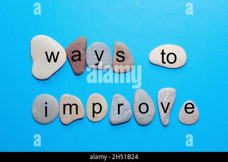 The phrase ways to improve stands as single letters on smooth natural stones with more natural colors against a blue background Stock Photo