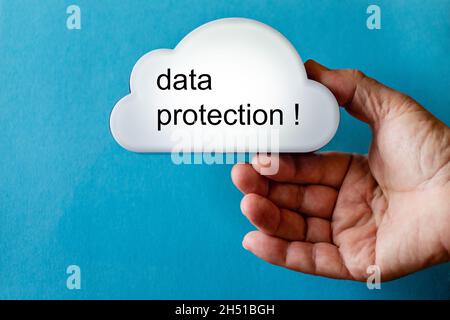 Hand holds a white cloud symbol against a blue background. The text is written on the cloud: date protection Stock Photo