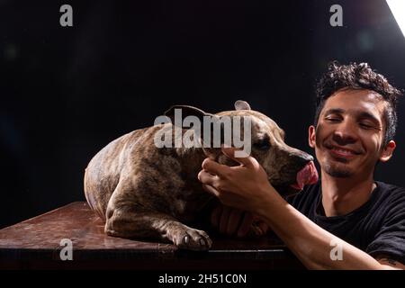 Latin man and his pitbull spending time together in a photo studio. Young adult and his pet love each other very much. Stock Photo