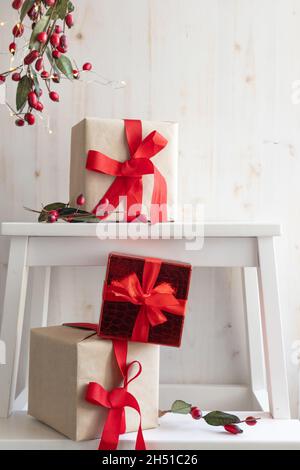 Christmas presents with red ribbon bows on a white background with border of branch with red berries and white lights with copy space Stock Photo
