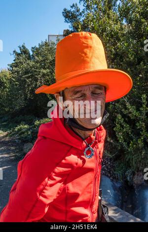 Rand, the street person, dressed in bright colors of red and orange, walks along State Street in Santa Barbara County with his very tall orange hat. Stock Photo