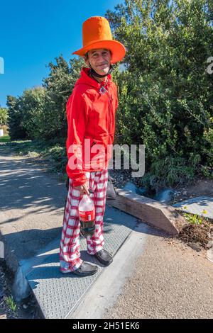 Rand, the street person, dressed in bright colors of red and orange, walks along State Street in Santa Barbara County with his very tall orange hat.