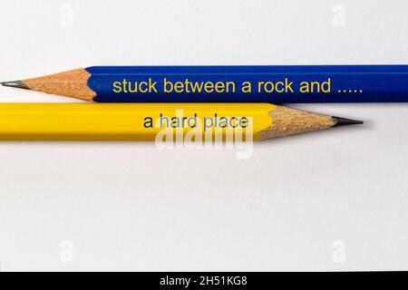 two sharpened pencils in blue and yellow point in different directions isolated against a white background with the conflicting wisdom: stuck between Stock Photo