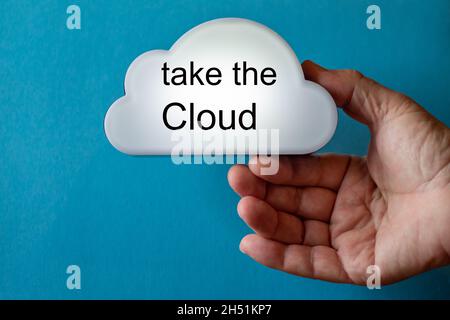 Hand holds a white cloud symbol against a blue background. The text is written on the cloud: take the cloud. Stock Photo