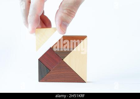 The missing building block is inserted into a tangram made of fine wood by a senior's hand from above Stock Photo