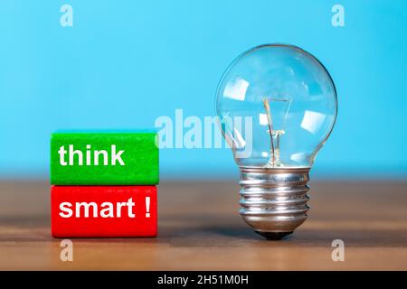 two blocks with the words think smart next to a free-standing antique light bulb against a blue background Stock Photo