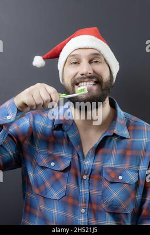 Smiling man in santa hat and checkered shirt holding toothbrush with paste near mouth Stock Photo