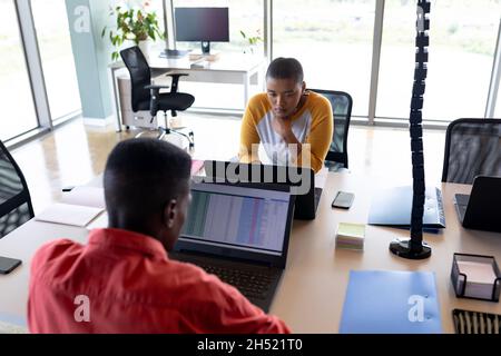 African american businesswoman and businessman working on laptops at desk in creative office Stock Photo