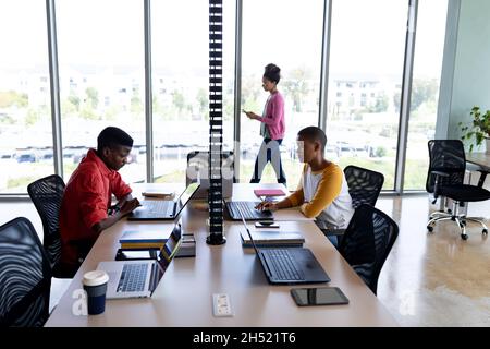 African american male and female colleagues working on laptops at desk in creative office Stock Photo