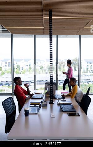 African american colleagues smiling while working on laptops at desk in creative office Stock Photo