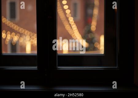 View from window outdoors at city square with decorated christmas tree, garland lights for new year Stock Photo