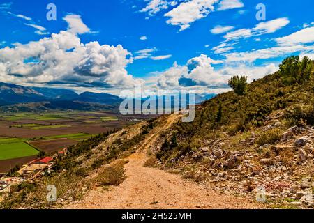 Mountain rocky path in Balkan mountains in Southeren Albania, Saranda, Vlora district in sunny hot summer day. Blue sky, white clouds. View to green f Stock Photo