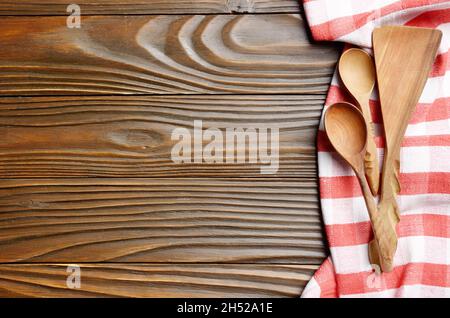 Red checkered napkin and wooden utencils on brown wooden kitchen table with copy-space. Top view Stock Photo