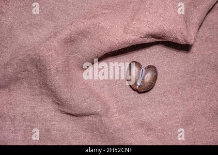 Malformed ripe brown and blue heart shaped plum with crack in middle on soft textured lilac linen material folded in unusual way as to catch the fruit Stock Photo