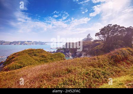 Seascape with the rocky shore in spring. View of Ria de Ribadeo del Eo bay. Puente de Los Santos bridge on the horizon. Ribadeo, Spain Stock Photo