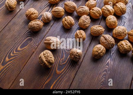 many walnuts with shells randomly scattered on brown wooden surface Stock Photo
