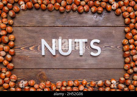 rectangular frame of many hazelnuts with shells on brown wooden surface with word nuts laid with silver letters Stock Photo