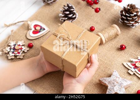 Christmas present in the hands of a child. Rustic christmas gift box with twine bow. Christmas decorations on table Stock Photo