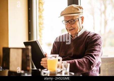 Senior man is sitting in cafe and using digital tablet. Stock Photo