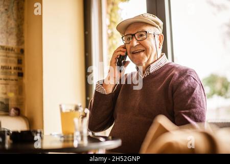 Senior man is sitting in cafe and talking on phone. Stock Photo