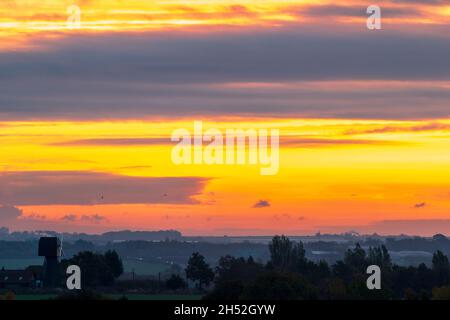 Yellow and orange dawn sky with clouds over a windmill without sails and trees in the Kent landscape in the autumn. Horizon low in the frame. Stock Photo