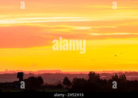 Yellow and orange dawn sky with clouds over a windmill without sails and trees in the Kent landscape in the autumn. Horizon low in the frame. Stock Photo