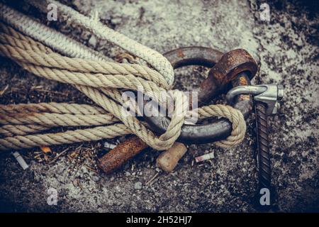 Old rusty metal mooring ring on the mooring wall with ropes tied to it. Stock Photo