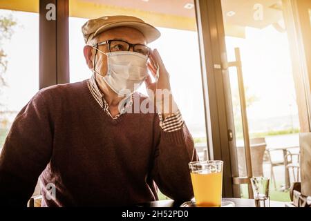 Senior man is sitting in cafe with face protection mask. Covid 19 prevention concept. Stock Photo