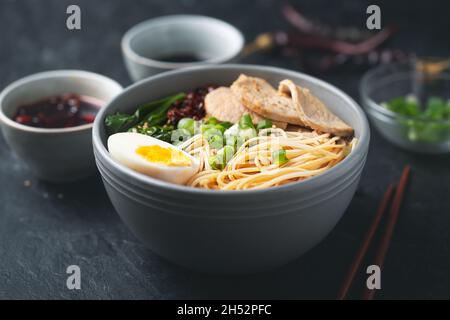 Ramen is asian noodles in a bowl with meat and vegetables or seafood, often flavored with soy sauce or miso. Dark background Stock Photo