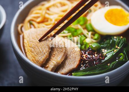Ramen with pork meat close up shot on a dark background, often flavored with soy sauce or miso, with toppings such as sliced pork, nori, menma Stock Photo