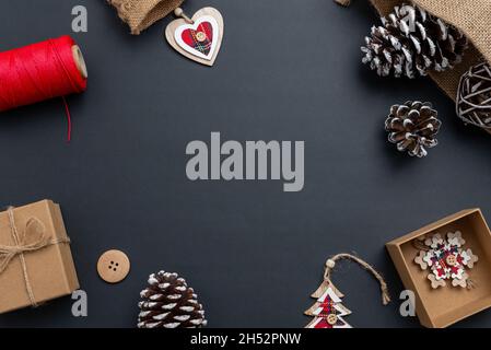 Christmas composition on black surface with red details on Christmas decorations. Christmas gift, pine cones, wooden decorations, red thread, tailorin Stock Photo