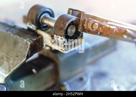 The metal product is squeezed in a vice at the workplace in the workshop. Workbench with old vises. Stock Photo