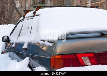 old abandoned broken car parked by the road under a large layer of snow on a cold winter day Stock Photo