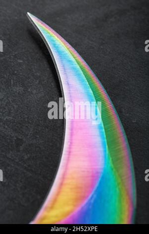 The sharp blade of the Kerambit knife made of steel is multicolored in close-up on a dark background. Cold steel, macro Stock Photo