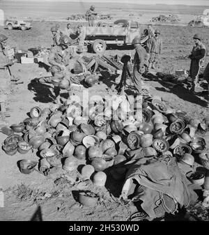 A vintage photo circa May 1943 of American soldiers piling up abandoned German helmets after the battle of Tunis and defeat of the German Afrika Korps Stock Photo